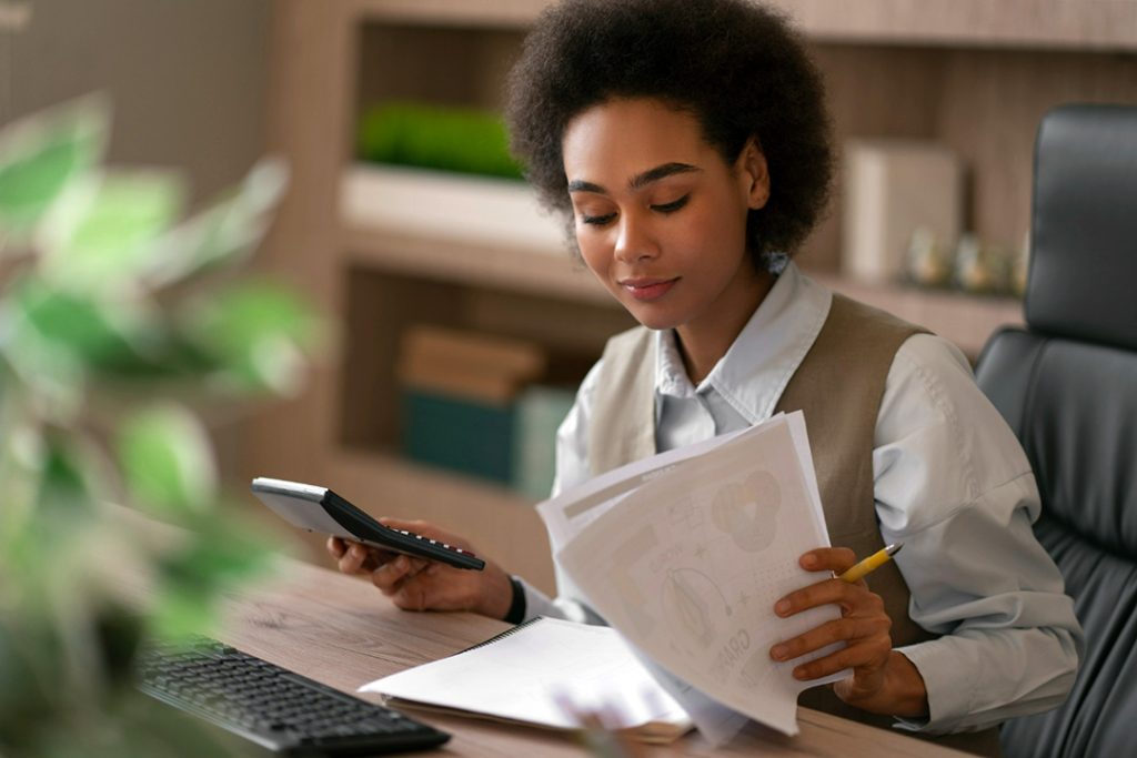 Young lady holding a calculator in one hand and looking at credit score papers in her other hand