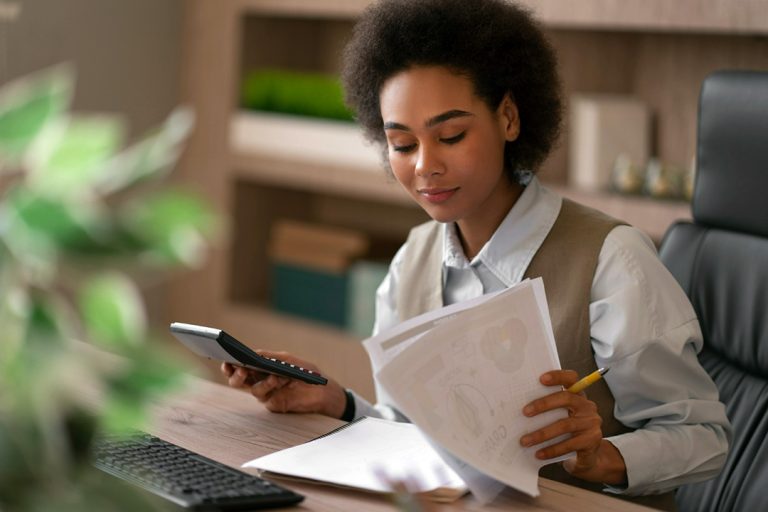 Young lady holding a calculator in one hand and looking at credit score papers in her other hand