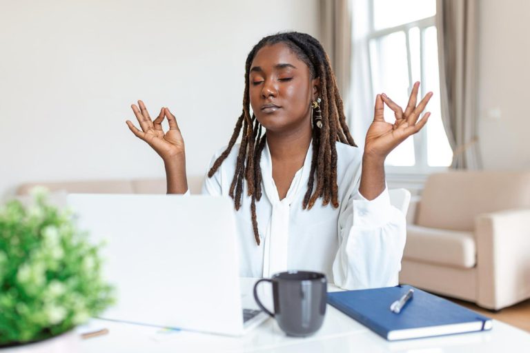 A woman meditating at her laptop while going through debt management books