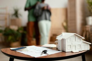 A model house sitting on a table next to a set of house keys and a mortgage document.
